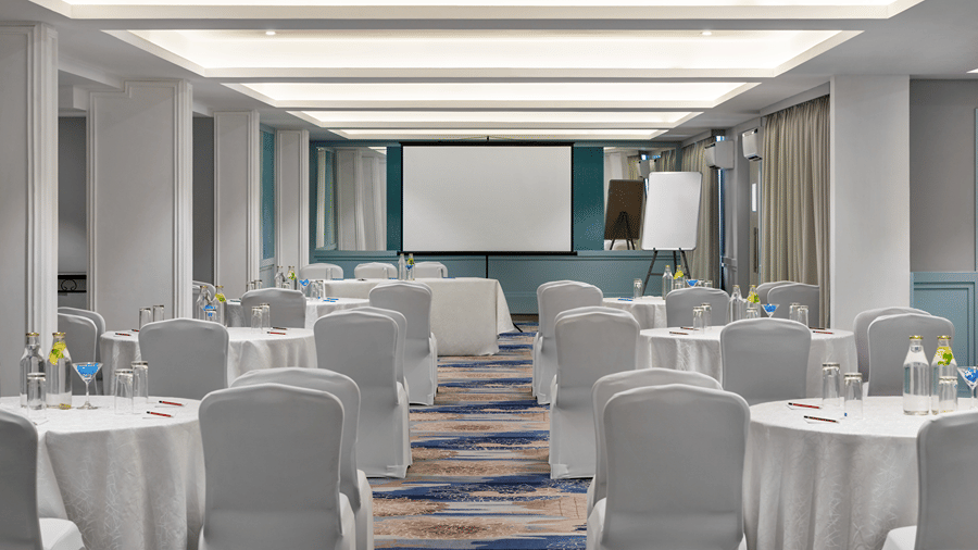 Event hall arranged with round tables, chairs and a presentation screen.