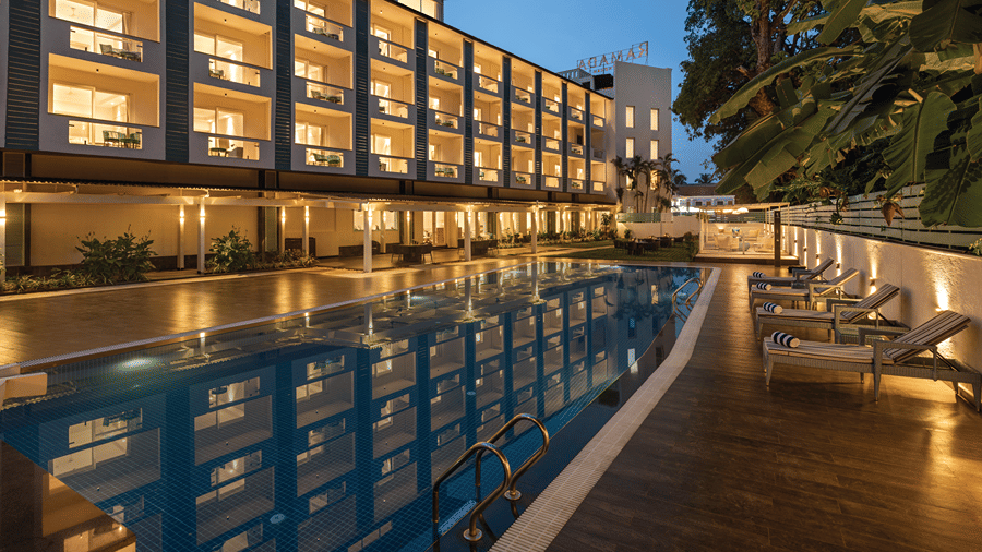 Outdoor swimming pool illuminated beside the hotel building at dusk.
