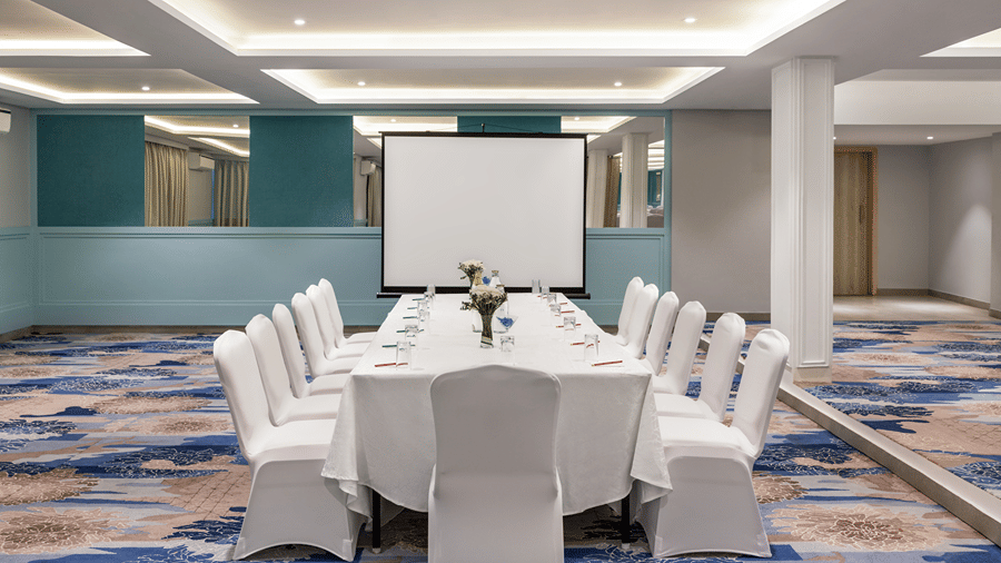 Meeting space arranged with a central table setting, chairs and a presentation screen.