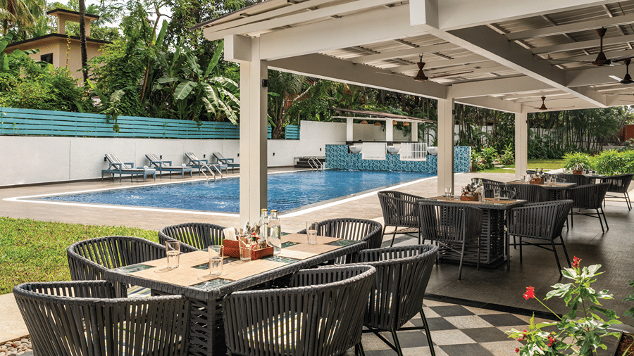 Outdoor poolside dining area with tables, chairs and tropical greenery.