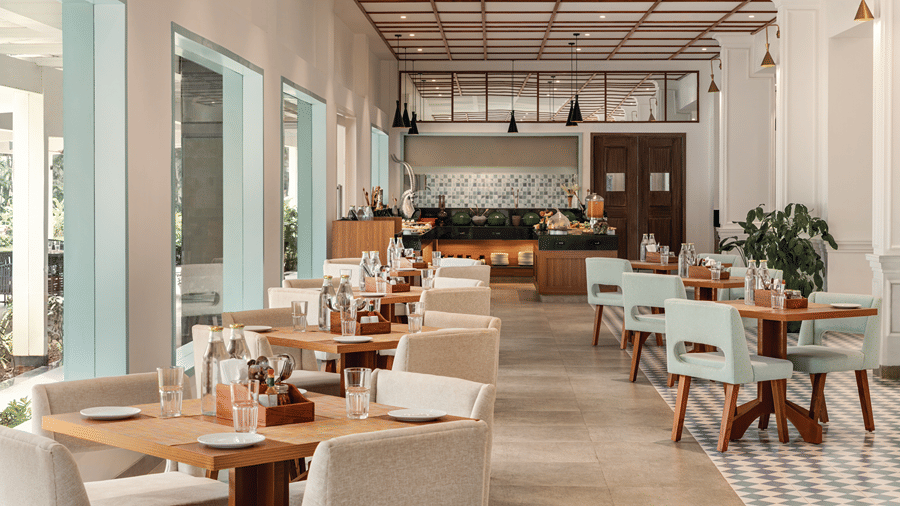 Bright restaurant dining area with wooden tables and chairs overlooking greenery.