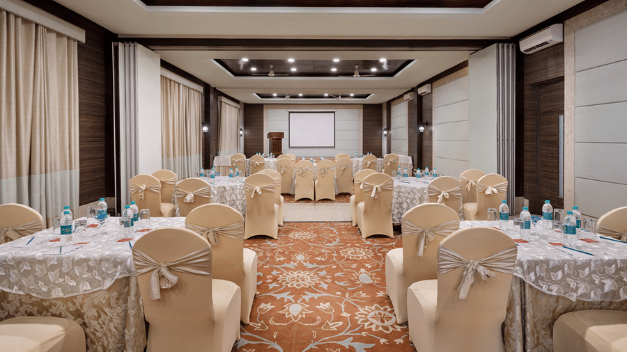 Multiple round dining tables set with white tablecloths and chair covers, in a banquet hall at Ramada by Wyndham Mussoorie Mall Road.