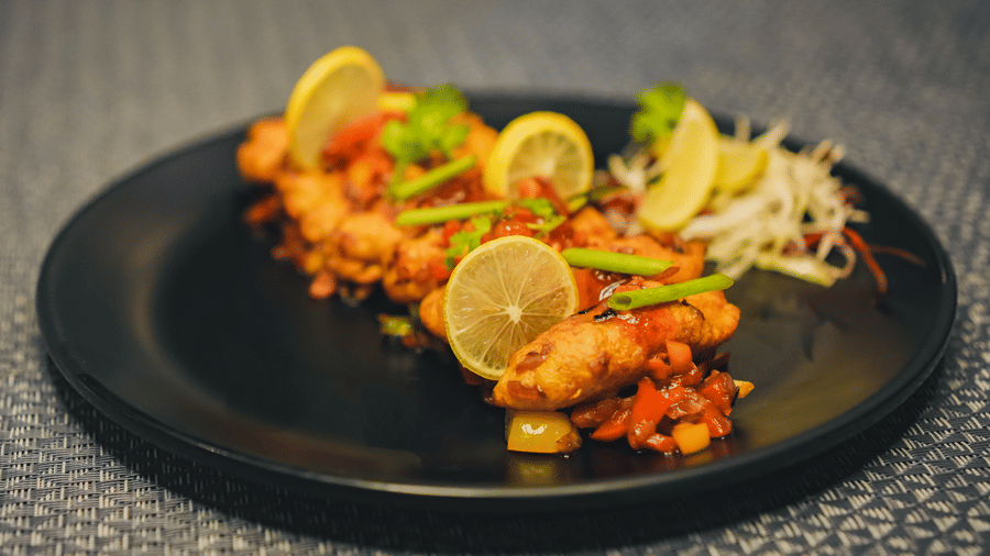 A plate of crispy fried fish starters beautifully garnished with fresh lemon slices and herbs, served on a black dish.