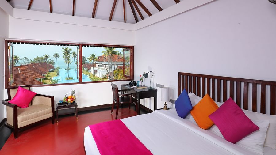 An image of a room featuring a wooden bed, decorative pillows, a sofa chair and a study desk - Rhythm Kumarakom