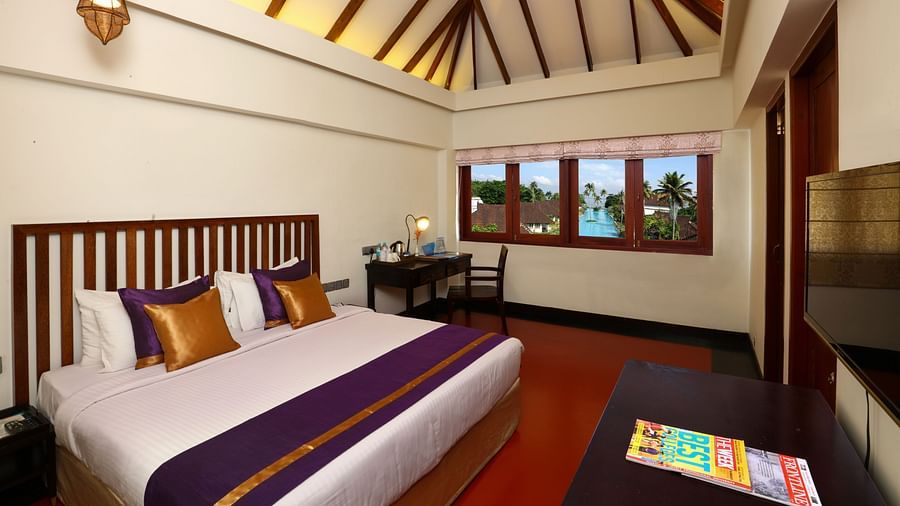 An image of a room consisting of a wooden bed, a TV and a seating space -Rhythm Kumarakom