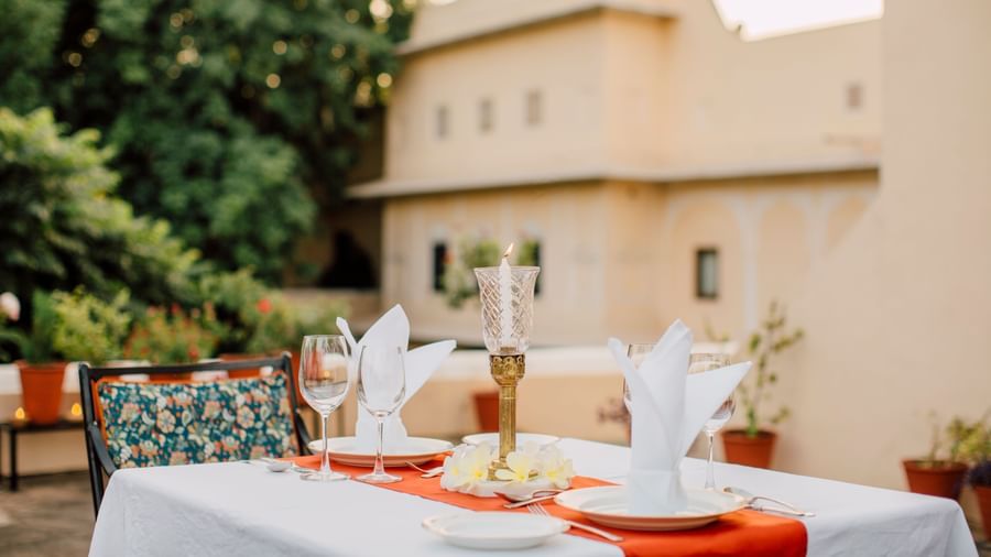 An outdoor dining setup at Royal Heritage Haveli with a table and chairs in the foreground and a light-coloured building in the background.