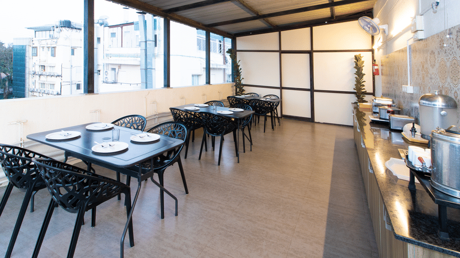 Open-air rooftop dining terrace with black chairs, dining tables, and a city backdrop at Sanctum Suites Indiranagar, Bangalore.