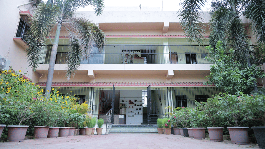 A multi-story building exterior at Shophori Wellness Retreat, Bolpur, framed by palm trees and potted plants.