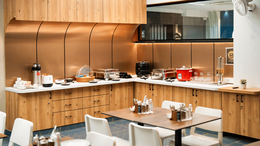 Buffet area with various dishes displayed, and tables with chairs neatly arranged in front at Sunrise Business Hotel, Hyderabad.
