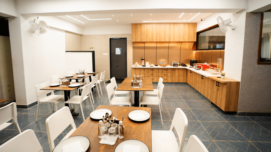 View of the restaurant with dining tables and chairs set, and a buffet counter in the background at Sunrise Business Hotel, Hyderabad.