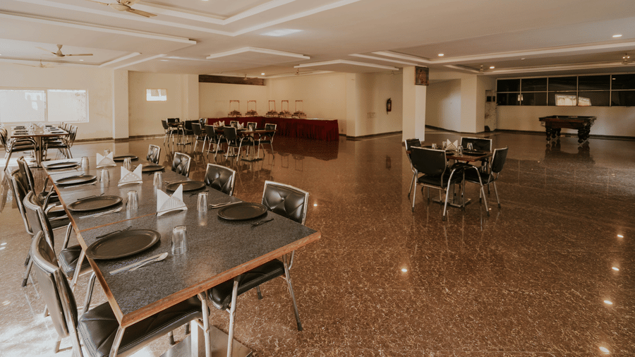 An indoor dining hall at TGI Jahaj Mahal, Mandu featuring dining tables with chairs over a polished reflective floor.
