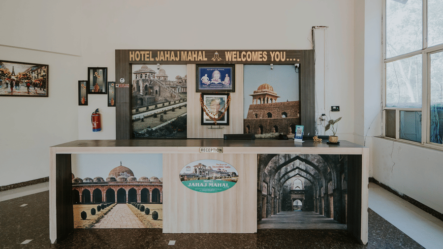 A reception desk at TGI Jahaj Mahal, Mandu with picture panels under a sign that reads 'Hotel Jahaj Mahal Welcomes You'.