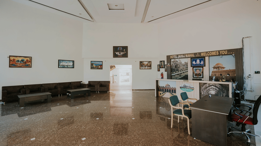 A wide view of a lobby area with a reception desk, office chairs, and framed pictures on the wall at TGI Jahaj Mahal, Mandu.