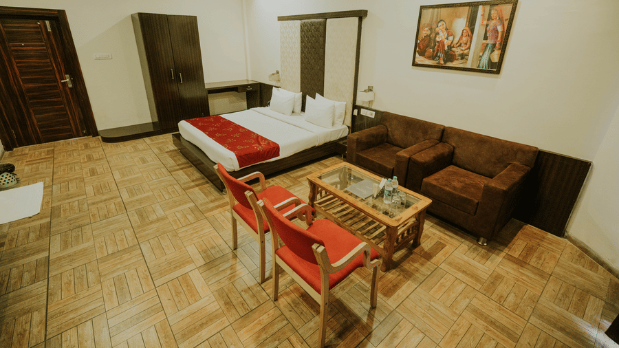 A bedroom at TGI Jahaj Mahal, Mandu, featuring patterned floor tiles, a king size bed, a wooden table, chairs, and a sofa.