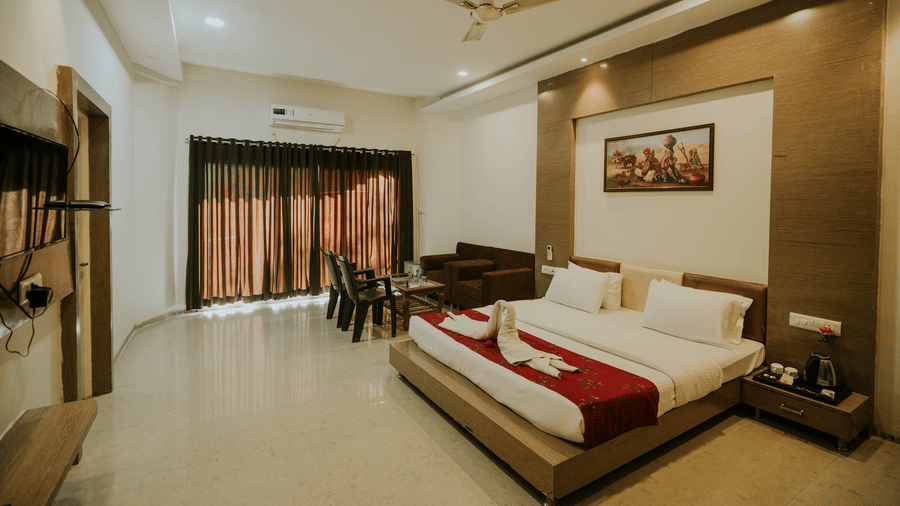 A bedroom at TGI Jahaj Mahal, Mandu, with a king size bed with a red accent, curtains, a ceiling fan, sofa, and a flat-screen television.