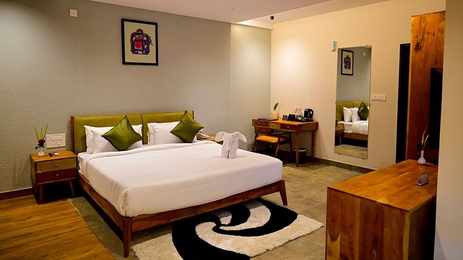 Hotel room with a large bed, olive green pillows, a unique black and white rug, and wooden furniture at TGI Livancia Hillside, JC Nagar, Mysore