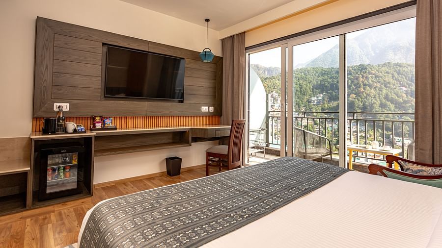 An image of a room with bed, flat screen TV, and an expansive glass door leading to the balcony - The Belvedere Himalayan Retreat, McLeodganj