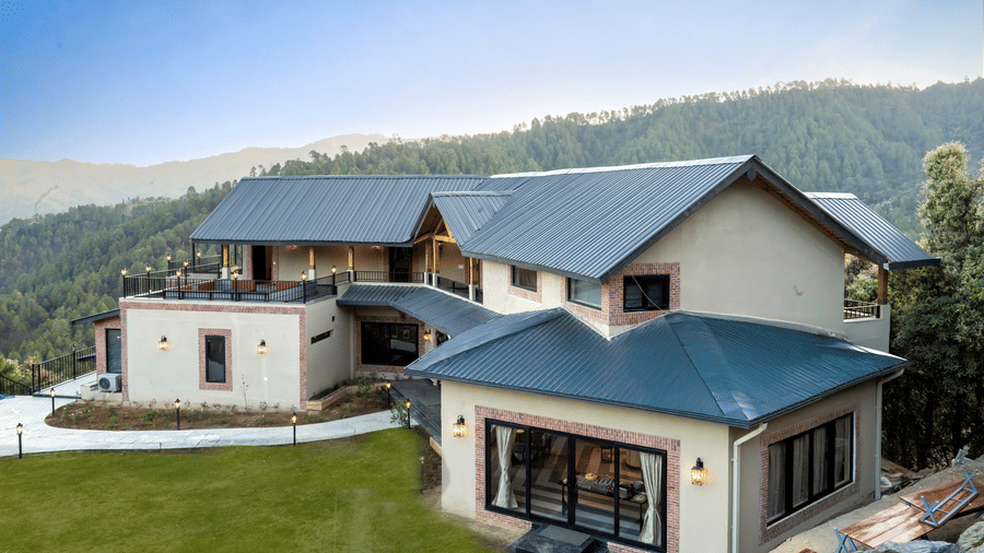Front elevation with grey pitched metal roofs, brick-trimmed cream walls, lantern lights, sliding glass doors and a lawn with path lights at The Chamomile Estate.