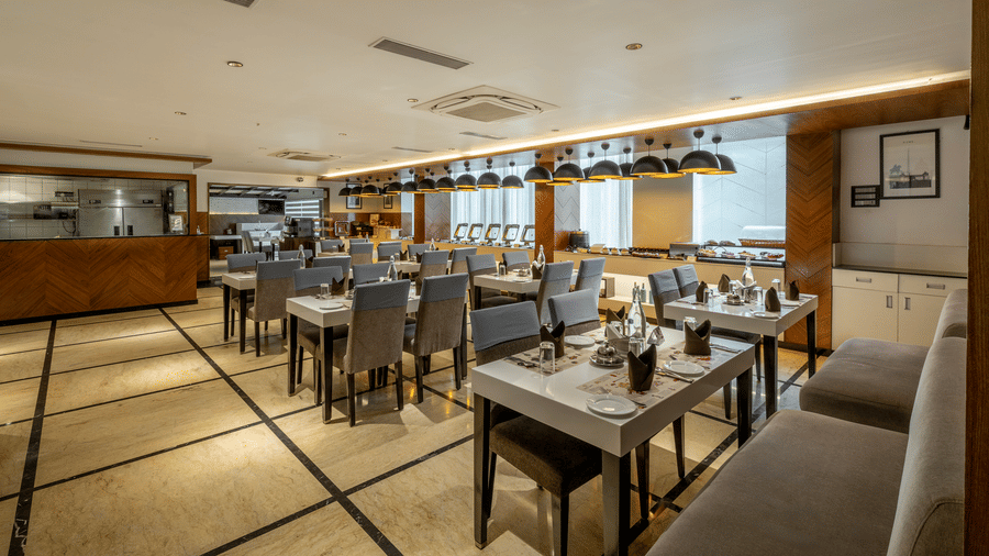Restaurant interior at The Citrine, Bangalore, with white-topped dining tables, grey chairs, buffet counter, and dome pendant lights.