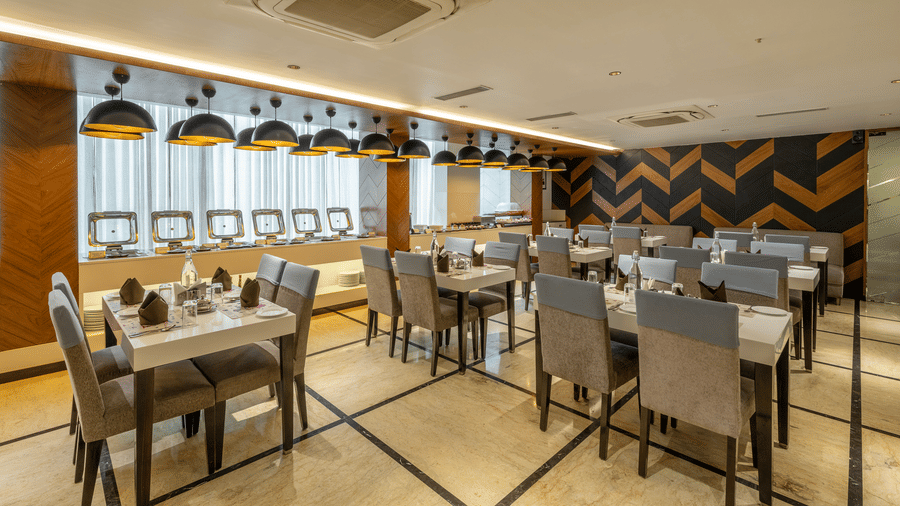 Restaurant at The Citrine, Bangalore, with white tables set for dining, grey chairs, chevron wall panelling, and a row of dome pendant lights.