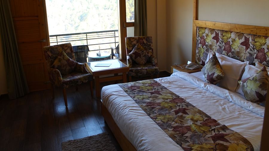 A cosy room with a large bed, floral-patterned bedding, and a seating area by the window at Dagshai Manor Kasauli - Inde Hotels.