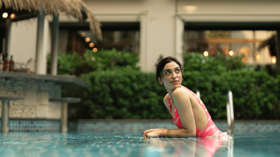 A woman standing in a swimming pool with water up to the chest, with a building structure, plants, and a thatched roof visible behind at The Evren, Vagator.