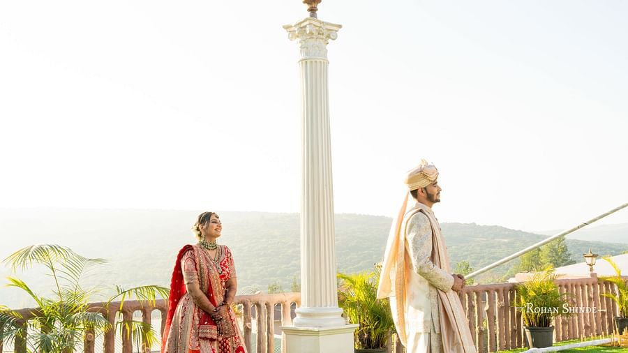Bride in lengha and groom in sherwani stand apart near a lamppost on a sunny balcony overlooking a landscape - The Grand Legacy Resort and Spa