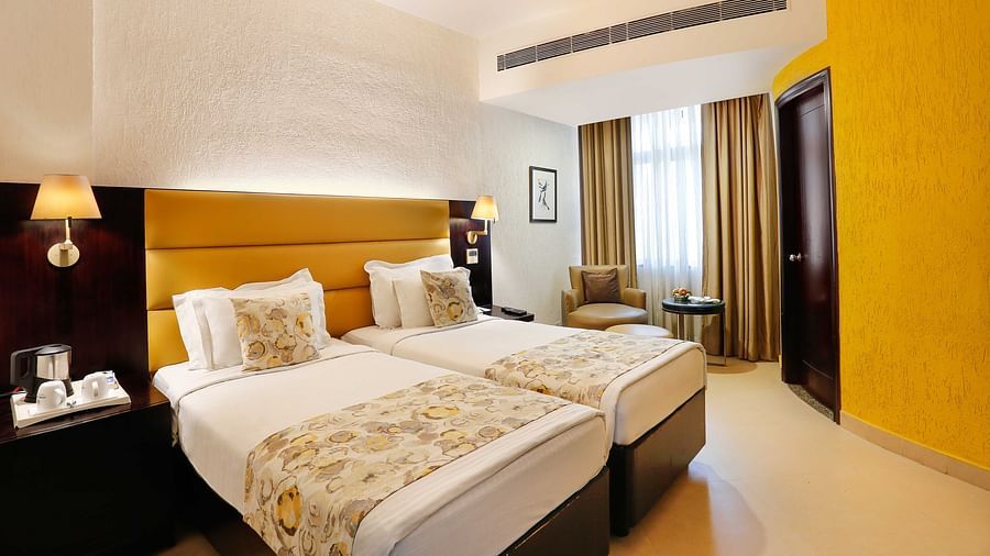 A spacious twin bedroom at The Manor, Bareilly, featuring two neatly arranged single beds and a window that fills the room with natural light