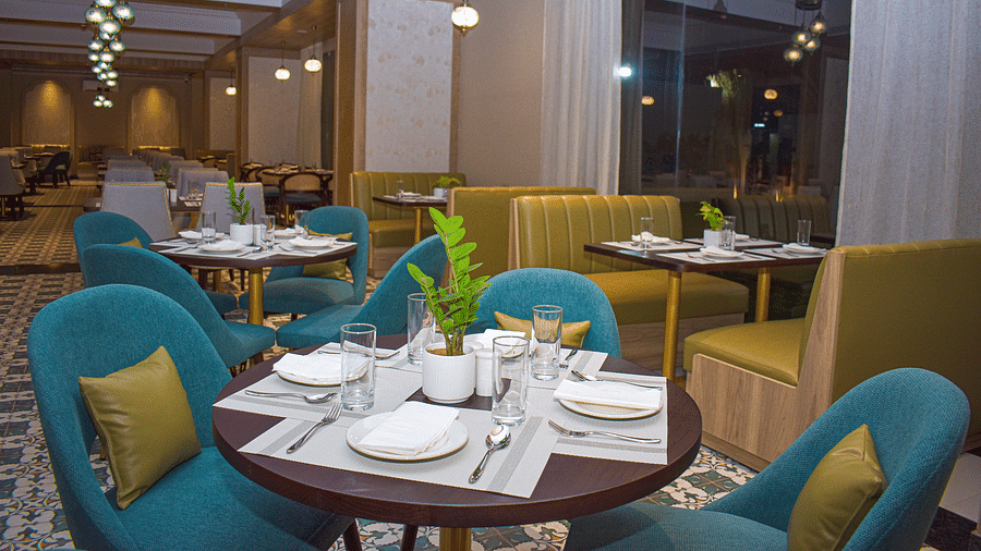A restaurant interior with teal armchairs, booth seating, round tables, a patterned floor, sheer curtains, and hanging pendant lights - Urban Suites by BluSalzz, Jaipur