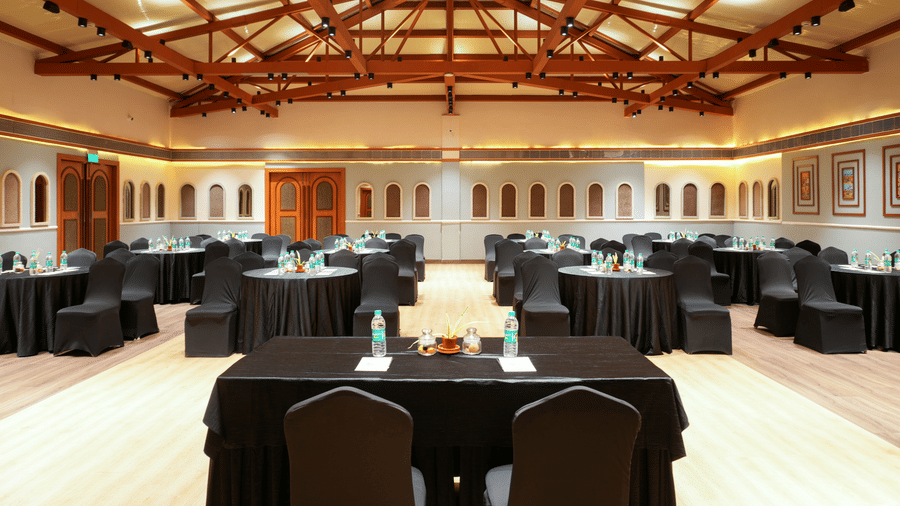 Expansive event hall at Vedic Village Spa Resort with round-table arrangements, high wooden ceilings, and ample space for corporate functions and celebrations.