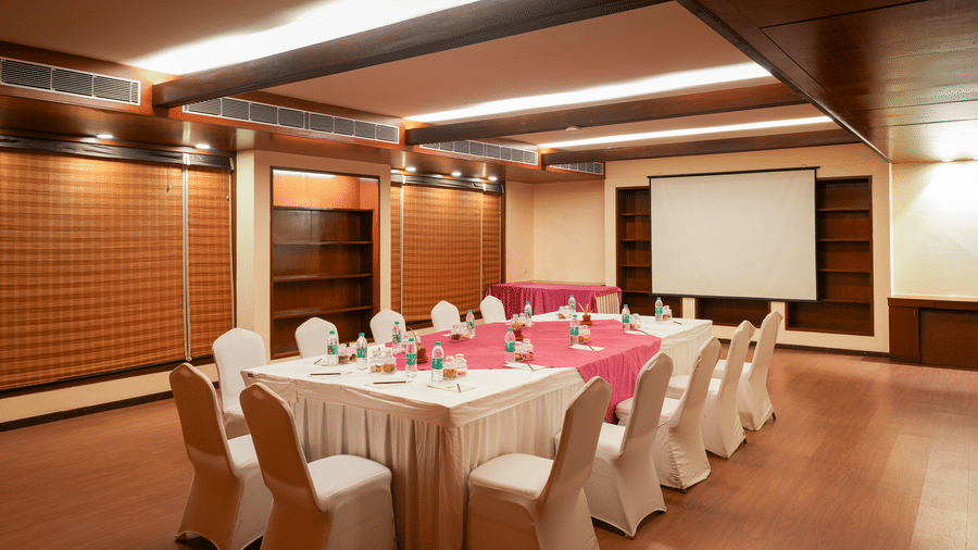 Professional meeting room at Vedic Village Spa Resort featuring conference-style seating, presentation screen, wooden paneling, and warm ambient lighting.