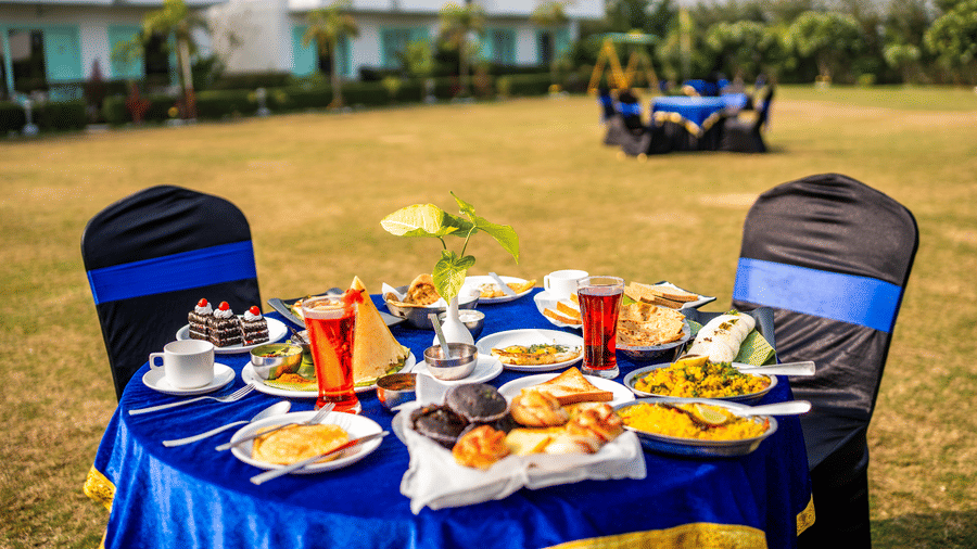 Outdoor breakfast setup at the lawn of  Vedikant Resorts The Mallard Corbett featuring a round table with several food items.
