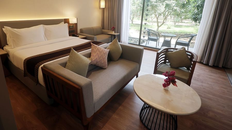 Cosy bedroom with outdoor views, soft grey curtains, and a plush bench at the foot of the bed at Wyndham Garden.