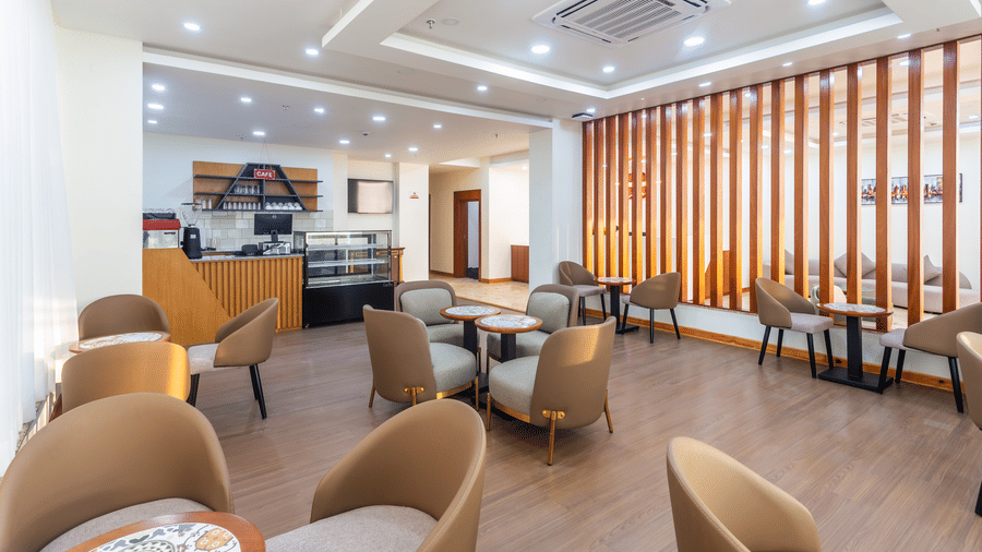 Lounge and service area of L Cafe at Mandala Norling Lords Prime Kathmandu, showing various seating arrangements and decorative wooden dividers.