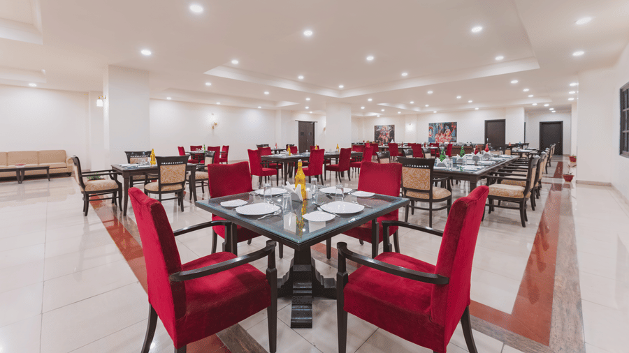A closer view of a dining table at the best restaurant in Nathdwara, Shri Vallabh Vilas Lords Plaza, featuring red chairs and tableware in a well-lit dining space.