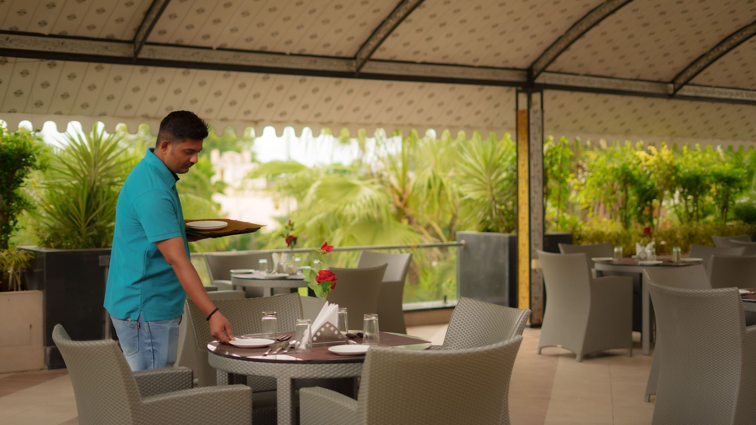 Staff member setting a dining table in the covered outdoor restaurant area at Arawali Ananta Elite, Jaipur.
