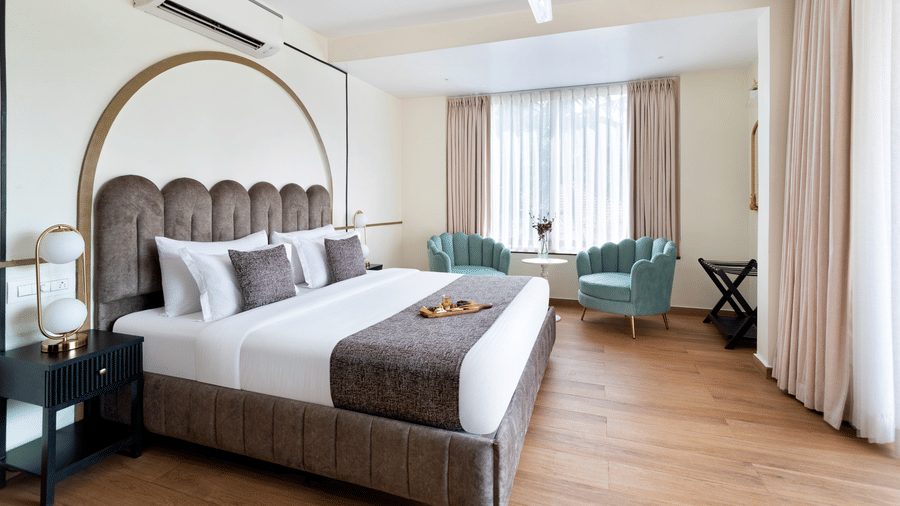 A daytime image of a room featuring a bed, two sofa chairs, a coffee table, a side table with a lamp, and a ceiling fan.