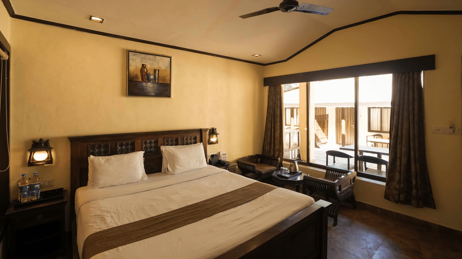 A room at Adamo The Village with a double bed, a large window, a seating area, and a side table with a lamp.