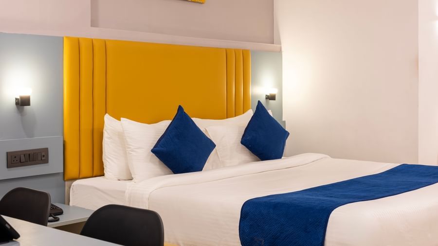 Close up side view of a modern Premium Room with a bed featuring blue accents, a work desk area, and a door on the left  - Beestay Hotels Financial District, Hyderabad 