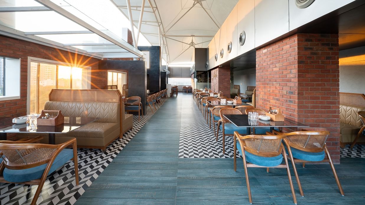 A restaurant interior with a long dining area lined with tables and chairs. The floor is tiled in a black and white geometric pattern - Clarks Inn, Indore