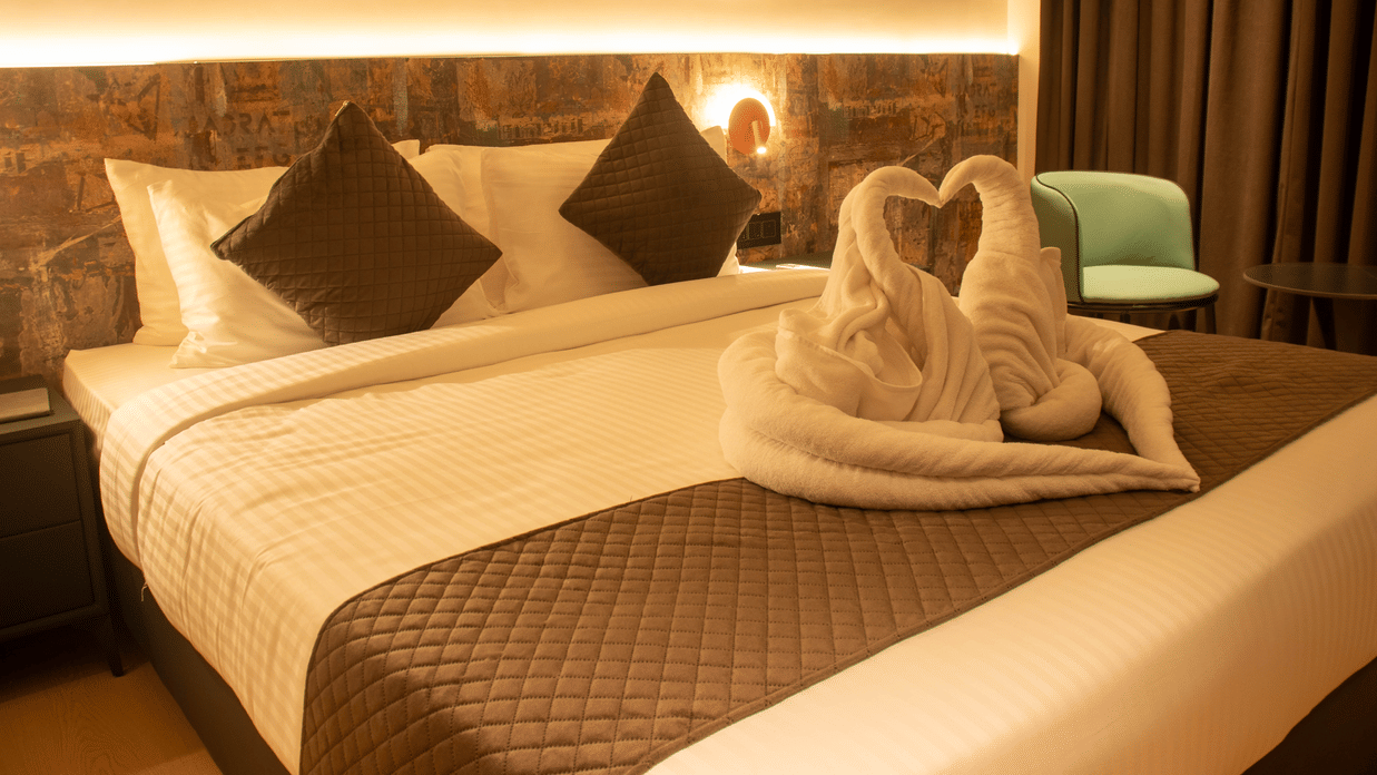 A bedroom with a king size bed with cushions, wall art, chair, bedside lamps, and towel arrangement on the bed at Magnus Lxia Premier, Kalyani Nagar.