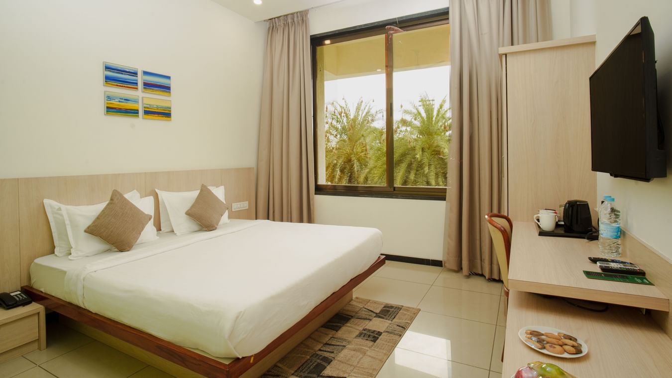 Clean hotel room featuring a large bed, minimalist wood furniture, and a sliding glass door at Arawali Ananta Elite, Jaipur.
