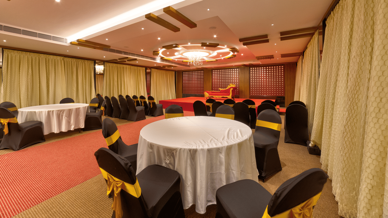 Round tables, black and gold chairs, a red carpet, and a stage setup inside the banquet hall of Icon Express By Bhagini, Mahadevapura.