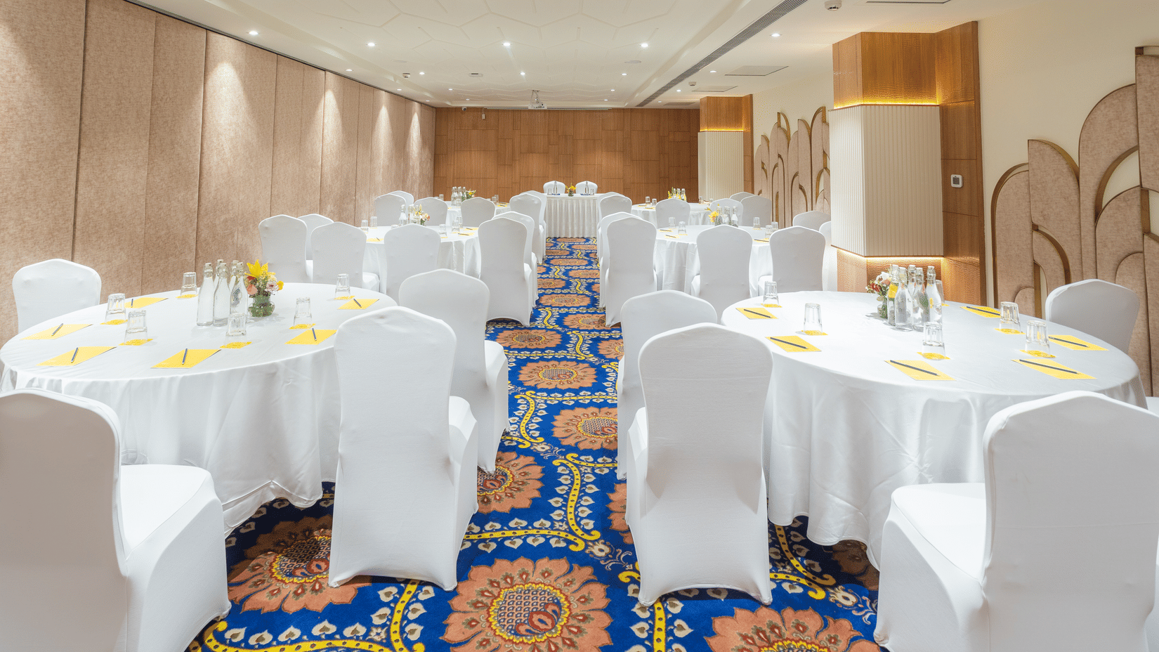 Cluster seating banquet setup at Golden Tulip Jaipur City Center with round tables, white chair covers, floral center pieces, and table settings for events and gatherings.