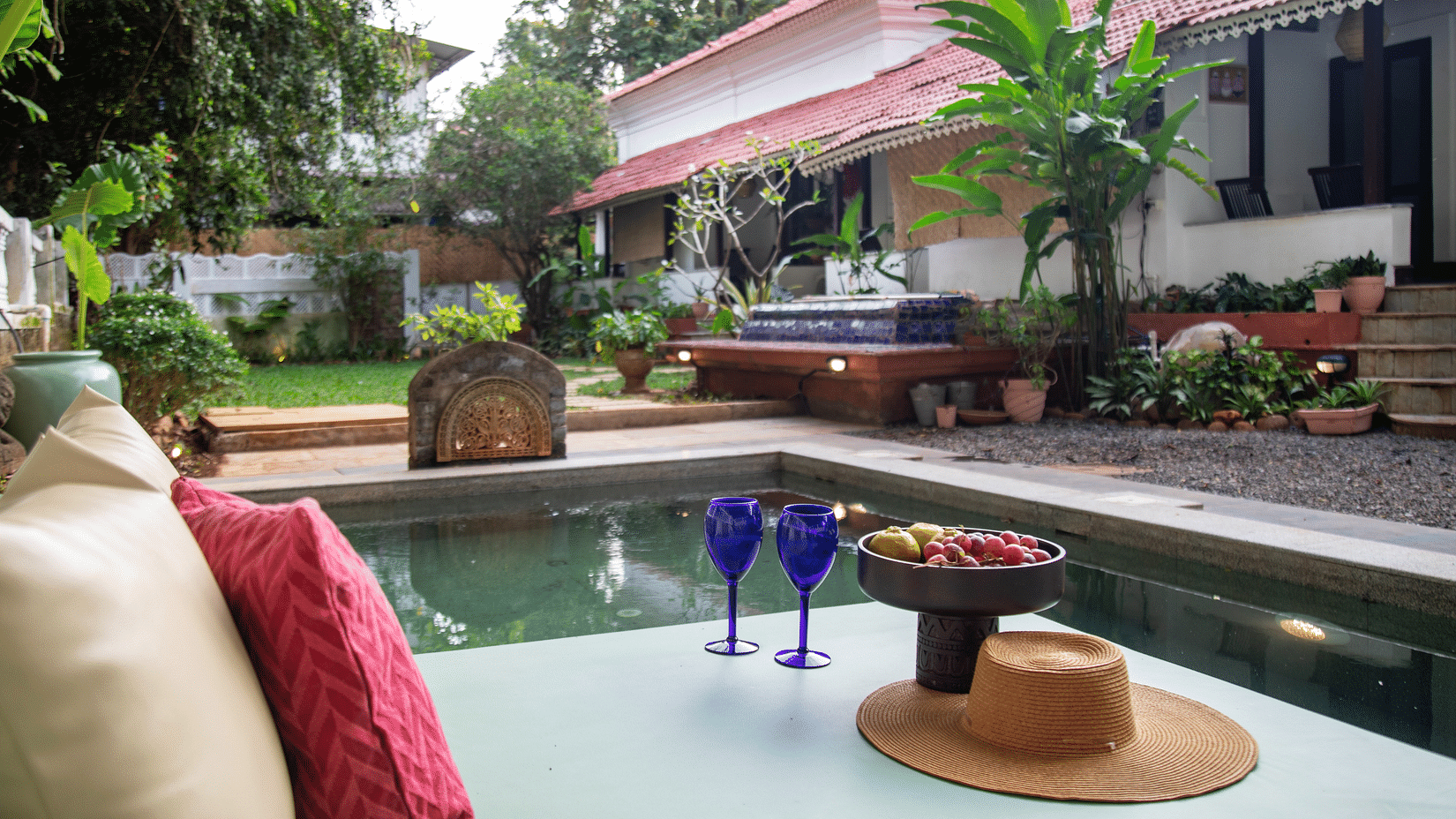 L shaped pool side with two blue wine glasses and surrounded by greenery @ Lamrin Ucassaim Hotel, Goa