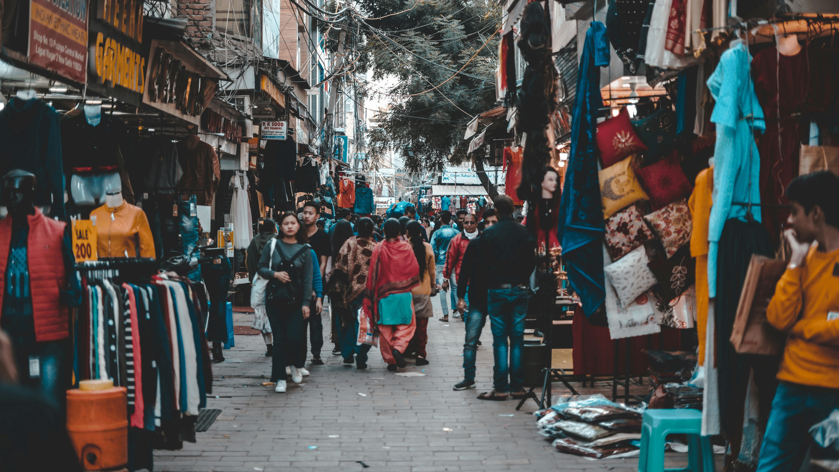 An overview of a crowded market street with people shopping and stalls on either side.