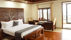 A side angle shot of the premium room featuring a king size bed, a seating area with two couches and a table  and a private balcony | A side angle shot of the suite at the resort feature a expansive balcony that overlooks the lush green valleys, king size 