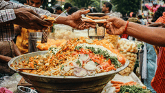 A street vendor serving a plate of Ghugni chaat to a customer at a busy food stall.