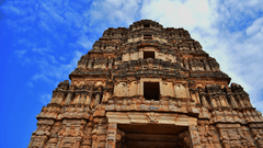 a Temple facade with intricate carvings of idols on top of it with blue sky in the background