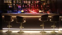 A stylish bar counter with glowing lights, featuring a wide selection of liquor bottles and two elegant stools, at Sarovar Portico, Sonipat.